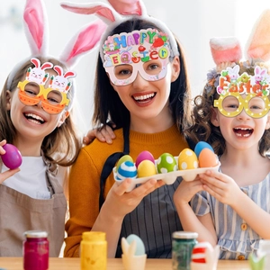 Three children and a woman wearing colorful Easter paper glasses while painting festive eggs