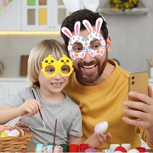Father and child wearing Easter bunny ears and chick party glasses while painting eggs