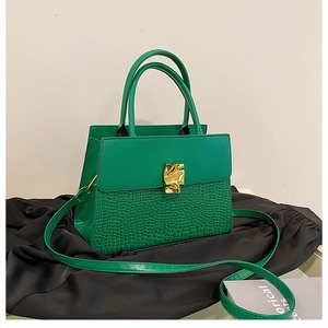 Detail of green faux leather handbag featuring crocodile texture and gold fold metal buckle