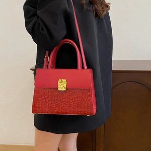 Red structural handbag with crocodile texture and gold metal lock held by a model