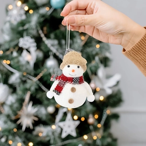 Cute plush snowman Christmas ornament with red plaid scarf on a warm lit Xmas tree