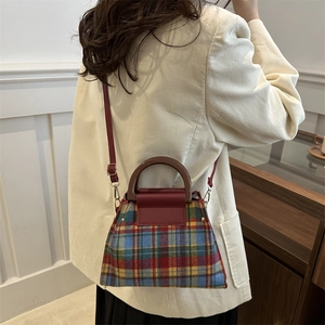 Chic plaid woolen handbag with red leather flap and brown handle worn by a model