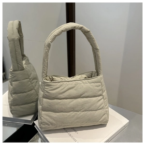 Detail showing the quilted puffer texture and wide handle of the beige padded handbag