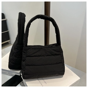 Close-up of a black quilted nylon puff bag with a wide handle on a white book surface