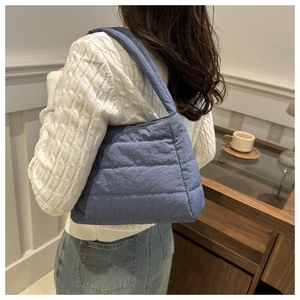 Detailed side view of a quilted puffer shoulder bag in fog blue nylon material