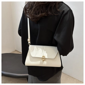 Detail of minimalist ivory crossbody bag with a golden circular buckle on a model