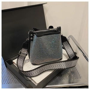 Détail d'un sac seau noir en strass avec une large bandoulière à chevrons sur une boîte