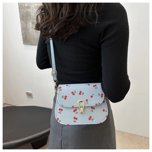 Detail of light blue crossbody bag with cherry prints and golden horseshoe lock