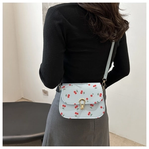 Détail du sac besace bleu clair avec imprimé cerises et fermoir doré sur un modèle