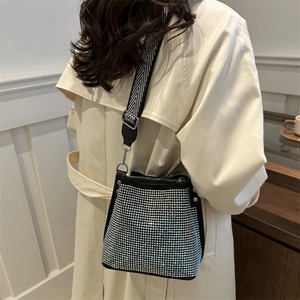 Sac seau scintillant en strass avec bandoulière géométrique porté par une femme en trench
