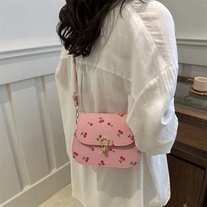 Mini sac selle rose à motif cerise avec boucle dorée porté par un modèle