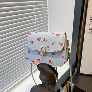 Sac bandoulière bleu avec imprimé cerises et boucle dorée en U en décor lifestyle