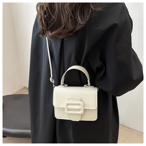 Detail view of cream white square crossbody bag with a large buckle on black outfit