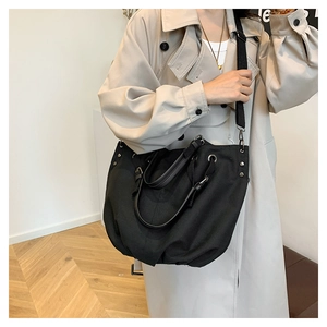 Side view of large black canvas workwear tote bag with rivets and wide strap on model