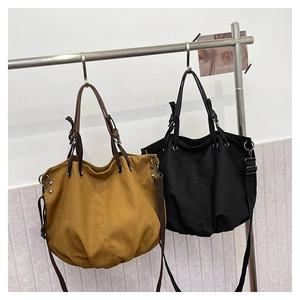 Detail of canvas tote bags in black and brown with adjustable straps hanging on a metal rack