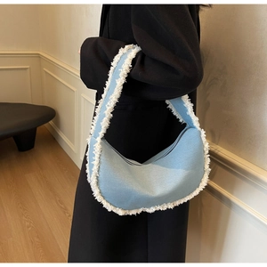 Detail view of light blue denim shoulder bag with white faux fur fringe on the model