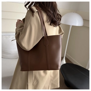 Detail of a large brown minimalist tote bag shown worn with a stylish beige trench coat