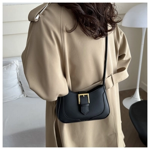Détail du sac croissant noir à boucle dorée porté sur un trench-coat beige élégant
