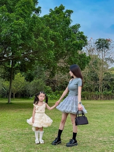 Mother and daughter in elegant off-white tulle skirts posing on a lush green lawn