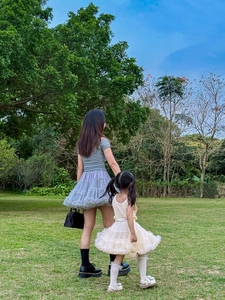 Elegant mother and daughter in layered tulle tutu skirts walking on green lawn