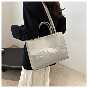 Detailed view of silver metallic tote bag with embossed lettering and shoulder strap on model