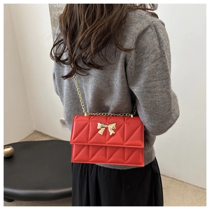 Sac bandoulière rouge matelassé avec nœud doré porté par un mannequin en pull gris