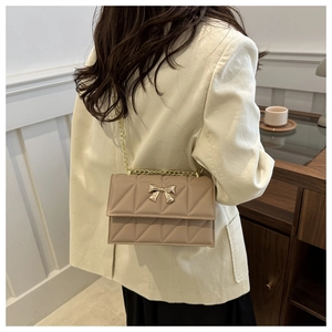 Détail du sac en cuir marron clair matelassé avec nœud doré et bandoulière chaîne
