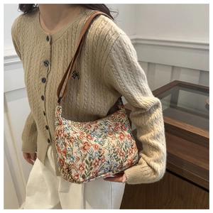 Floral tapestry crossbody bag with retro print details shown on a beige knit cardigan