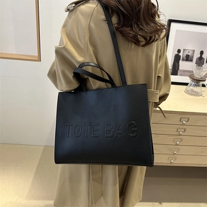 Large black textured tote bag with embossed lettering and long shoulder straps