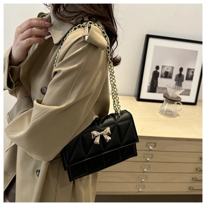 Détail du sac matelassé noir avec fermoir nœud doré porté sur un trench-coat kaki