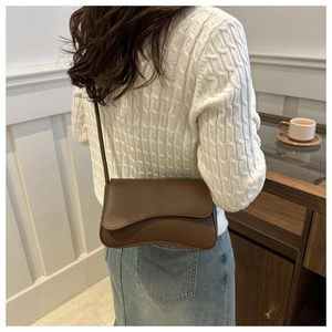 Detail of a dark brown crossbody bag with a curved flap and smooth matte leather finish