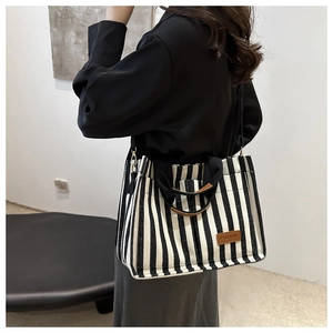 Detail of striped canvas tote bag showing fashion tag, web handles and shoulder strap