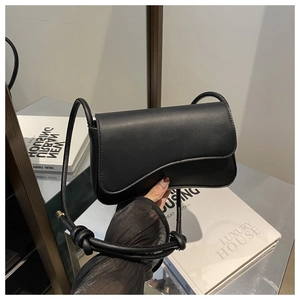 Detailed macro view of the black leather crossbody bag featuring an asymmetrical curved flap