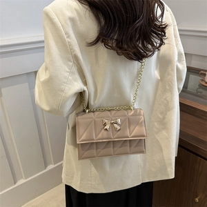 Sac bandoulière matelassé beige avec nœud doré et chaîne sur mannequin femme