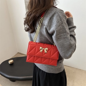 Sac bandoulière matelassé rouge avec chaîne dorée et nœud élégant porté par un modèle