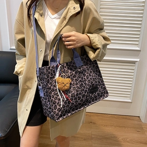 Large leopard print tote bag with blue handles and a yellow bear charm on model