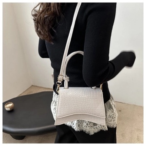 Detail of white crocodile embossed hourglass handbag with gold hardware and curved base
