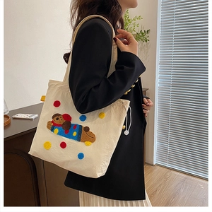 Gros plan du sac fourre-tout en toile blanc cassé avec broderie chiot et pompons colorés