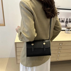 Petit sac à bandoulière noir minimaliste avec boucles dorées porté par un mannequin