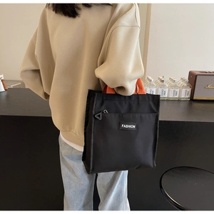 Detail of a black nylon handbag featuring contrast orange woven straps and side zipper pocket