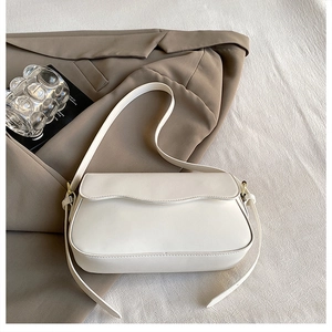 Détail d'un sac à bandoulière blanc avec bords ondulés posé sur un blazer marron