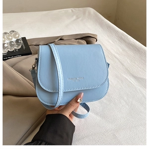 Detail view of sky blue saddle bag with flap cover and metallic hardware on fabric