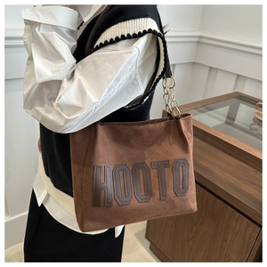 Detail of coffee brown suede tote bag with HOOTO leather patch and gold chain strap