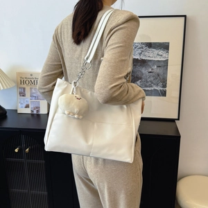 White faux leather tote bag with silver chain and plush charm worn by model in room