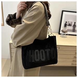 Close-up of black suede tote bag with HOOTD lettering and gold chain shoulder strap