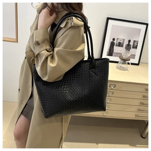 Close-up of model wearing black woven leather tote bag with elegant shoulder strap