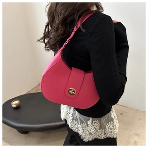 Close-up of rose red half-moon baguette bag with golden clasp worn on the shoulder