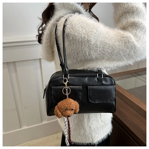 Detalle de un bolso de almohada en cuero negro con bolsillos y un colgante de caniche
