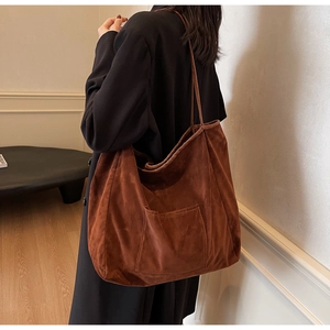 Detail view of large brown suede tote bag with front pocket shown on model's shoulder