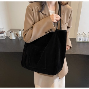 Detail of black corduroy tote bag with front pocket shown on model in cafe setting